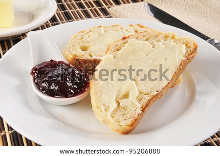 A plate of buttered bread and strawberry or blueberry jelly