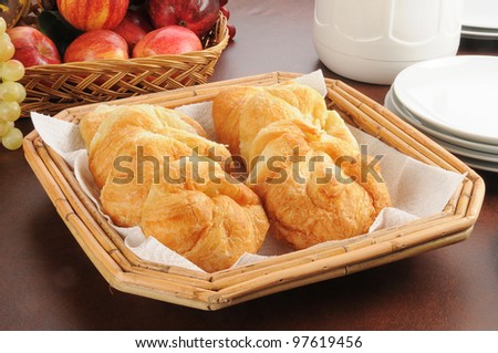 A basket of mini croissants, fruit, plates and a pot of coffee on a breakfast buffet