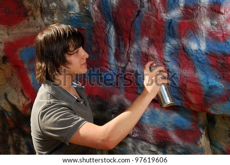 A teenager spray paints a graffiti covered rock
