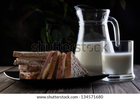 Sandwich and pitcher of milk. Dark tone.