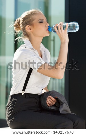 Young businesswoman drinking water from a small bottle