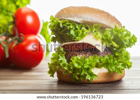 Cheeseburger with lettuce, onions and tomato in a sesame bun on wooden table