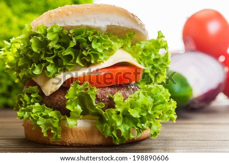 Cheeseburger with lettuce, onions and tomato in a sesame bun on wooden table