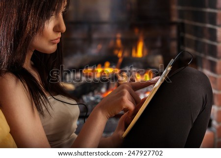 Young woman using digital tablet sitting by fireplace