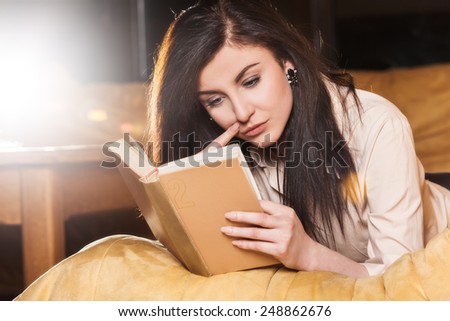 Young woman lying on her couch reading a book at home in the sitting room