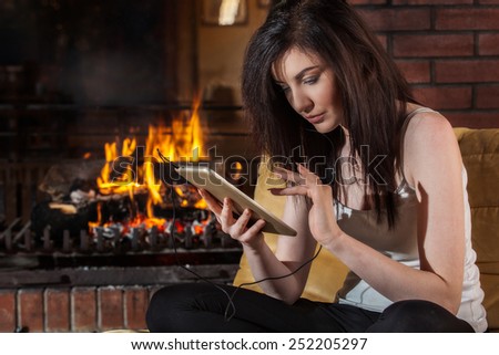 Woman using digital tablet sitting by fireplace