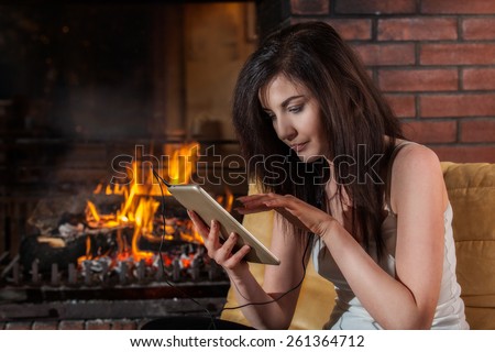 Young woman using digital tablet sitting by fireplace