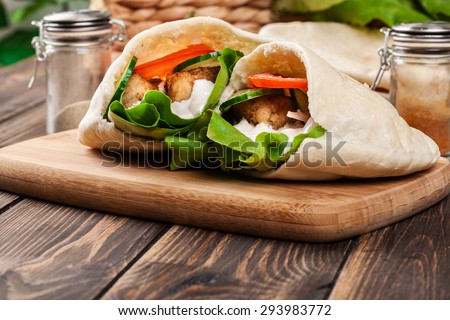 Pita bread with falafel and fresh vegetables on wooden table