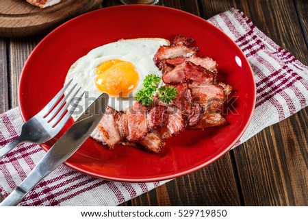 Slices of smoked bacon and fried egg on a red plate. Eating habits concept