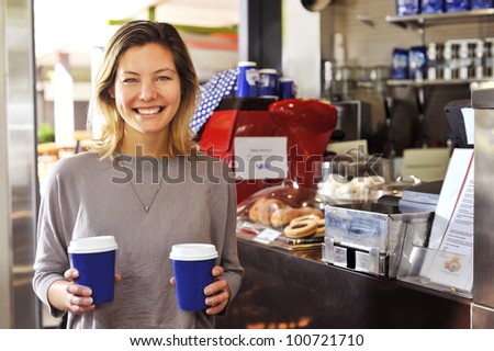 a young woman smiles to camera as she walks away from the cafe counter carrying her two coffees, part of my \