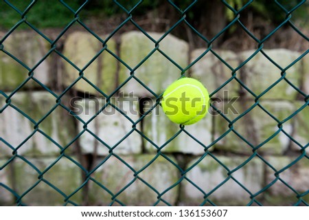 a ball stuck in a chain link wire fence at a tennis court