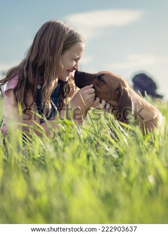 girl with her puppy in the grass, touching noses