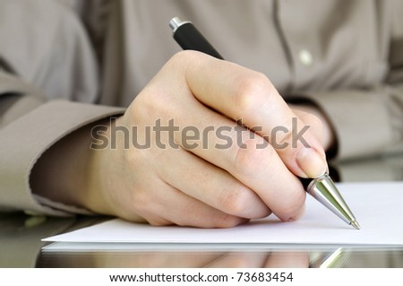 pen in hand writing on the white page and reflection