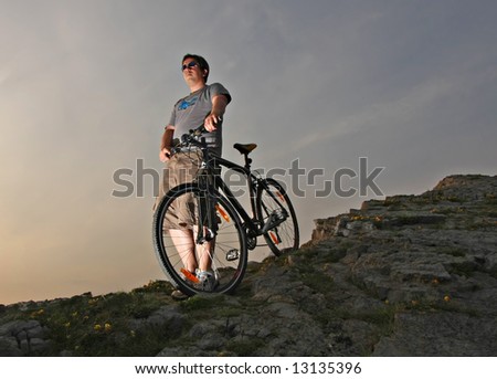 Young Man in Shorts with Hybrid Mountain bike on a rocky hill - Sunset with edgy lighting