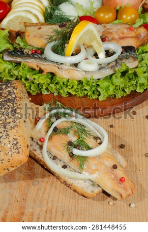 Smoked mackerel fillet, garnished with onion rings, in whole wheat bread, with lettuce on a wooden chopping board