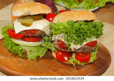 Hamburgers, fast food, burger, hamburger steak with salad, tomato, cheese, cucumber on a wooden chopping board