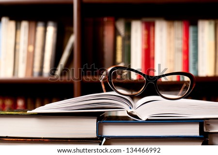 Eyeglasses lying on the opened book and many other books on background