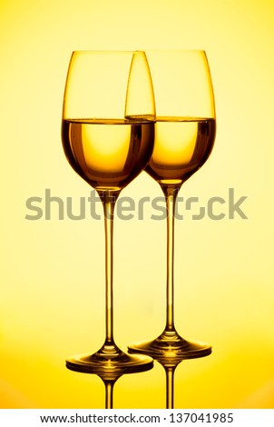 Two glasses filed with white wine on yellow background. Studio shot.