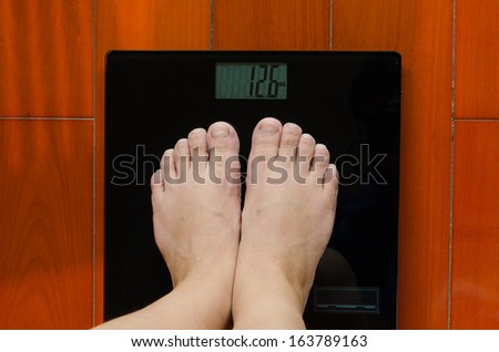 A girl standing on the weighing-machine to know how weight she is. this is part of the fit-keeping plan./Two feet on the weighing-machine