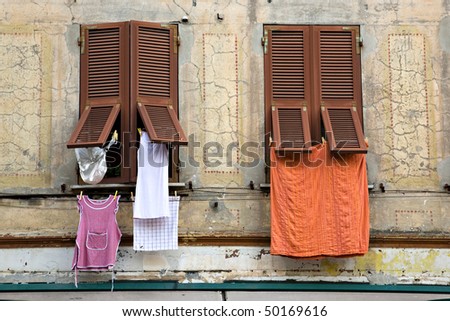 An old building with new brown shutters on the windows.  Various pieces of laundry are hanging from the windows.