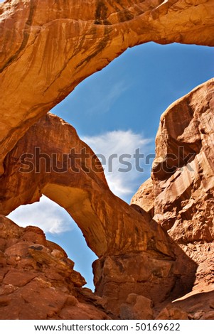 The red rock of Utah\'s Arches National Park, with blue sky and white clouds seen through one of the arches.