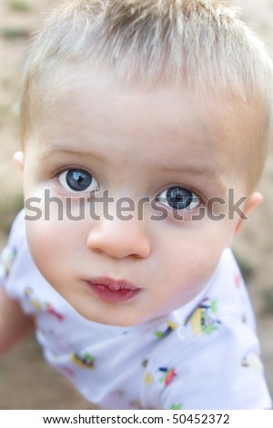 A young child looks up at the camera with big eyes and a curious expression.