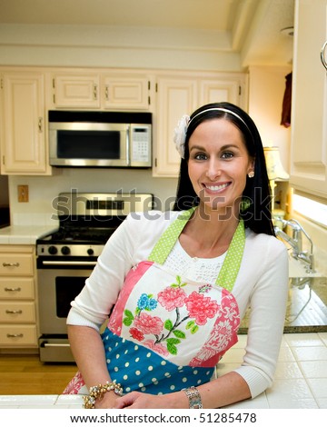 A pretty woman in a clean, modern, kitchen, leaning on the counter and smiling.