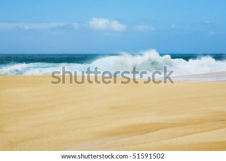 Golden sand and blue surf with a wave crashing along the shore in Hawaii.