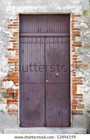 An ancient brick wall with a purple door on a street in Italy.