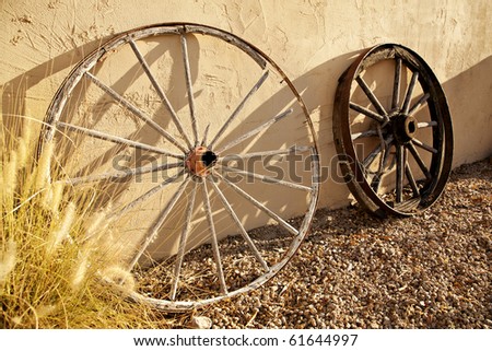 Two wagon wheels of the old American West, leaning against a stucco wall in the late afternoon sun.