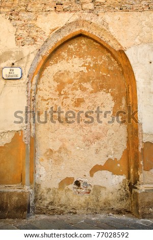 An ancient, run-down brick and stone wall in Italy with a filled-in archway and a sign reading \