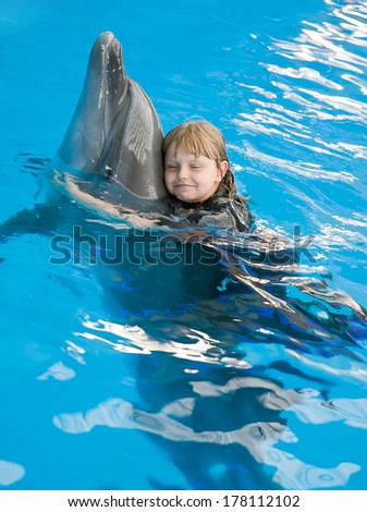 The small girl hugs a dolphin at the dolphin therapy session