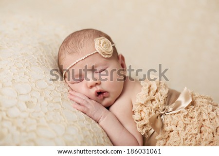 newborn baby girl wearing a  flower headband curled up and asleep on a textured blanket.