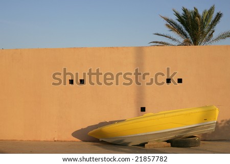 boat outside ocean behind wall blue, yellow, shadows composition