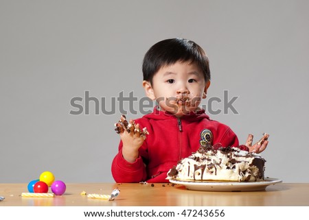 A cute Asian kid posing with his birthday cake, looking innocent, making a mess out of the cake,