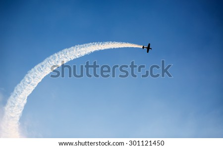 Silhouette of an airplane performing acrobatic flight on blue sky. Trace of Smoke behind