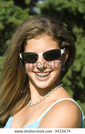 Pretty teenage girl with braces smiling outdoors wearing sunglasses.