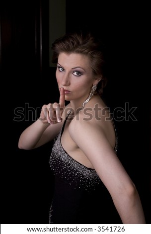 Beautiful brunette woman looking back through a door with her finger on her lips indicating a secret.
