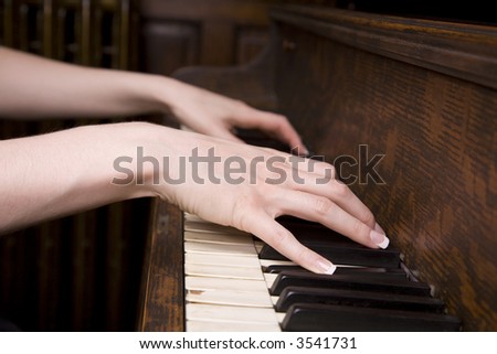 Woman's hands on an old piano playing a song. Focus is on the closer hand.