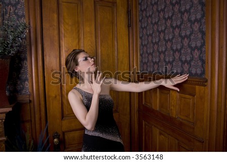 Beautiful young brunette woman in an evening gown looking critically at the woodwork on a wall.