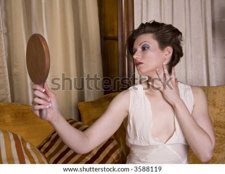 Beautiful young brunette woman wearing a vintage slip admiring herself in the mirror.