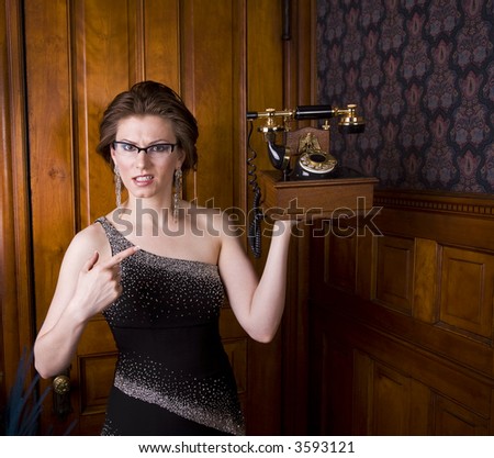 Beautiful young brunette woman wearing an evening gown looking perplexed at an old fashioned telephone. See my portfolio for more like this.