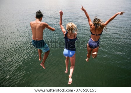 Teenagers in swimsuits leaping into lake from high up on sunny summer day
