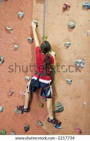 A young girl climbing a tall, indoor, man-made rock climbing wall