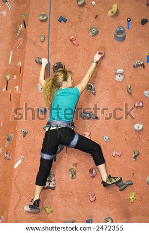 Pretty, young, athletic girl climbing on an indoor rock-climbing wall