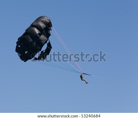 Man parasailing through the air with a black chute against a blue sky