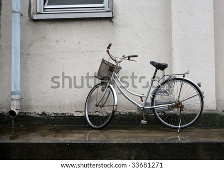 Silver Japanese city bicycle with basket parked along a wall during a rain stork in Tokyo, Japan.