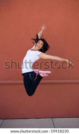 Young attractive girl jumping for joy on a sidewalk with a red wall background