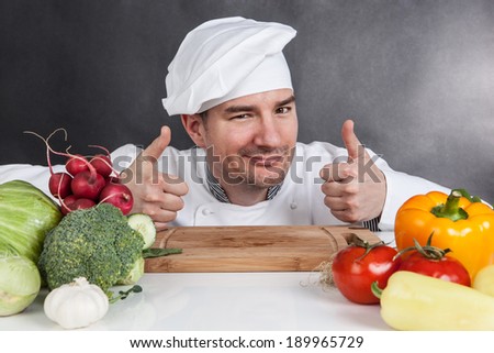 Young chef with OK sign and vegetable on black background