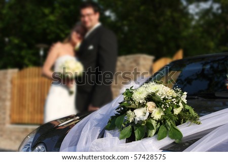 Wedding car decorated with flowers. Bride and groom standing near car.